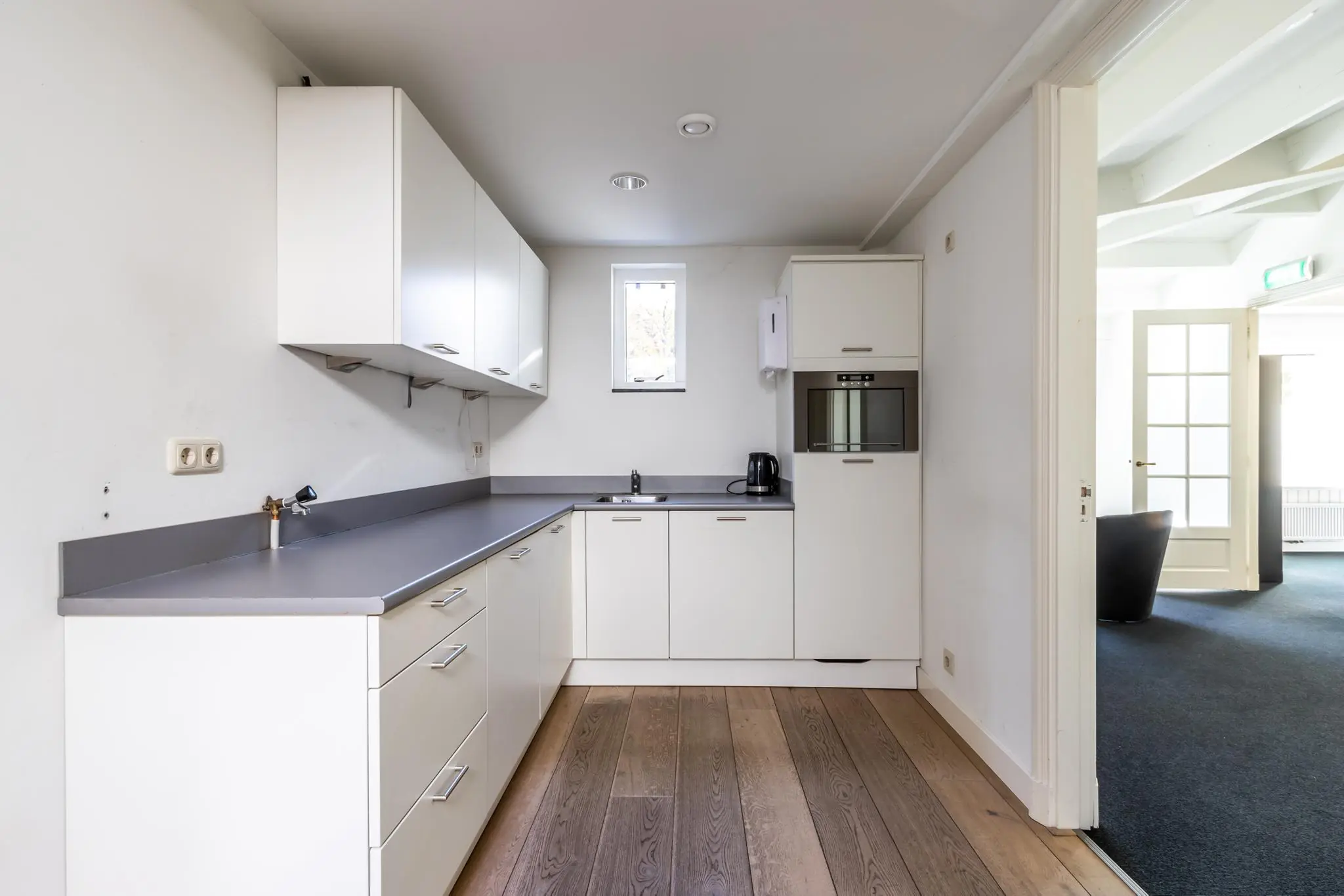 Moderne, witte hoekkeuken met inbouwapparatuur en houten vloer aan de Langbroekerdijk A.